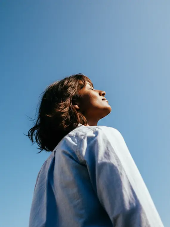 A woman outdoors looking up toward a bright blue sky
