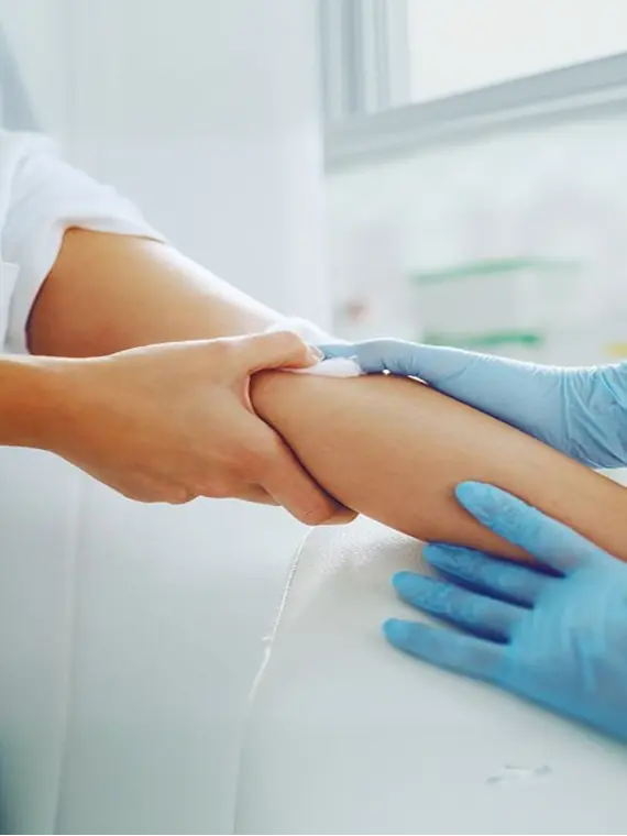 A clinician's gloved hands drawing a blood sample from an arm